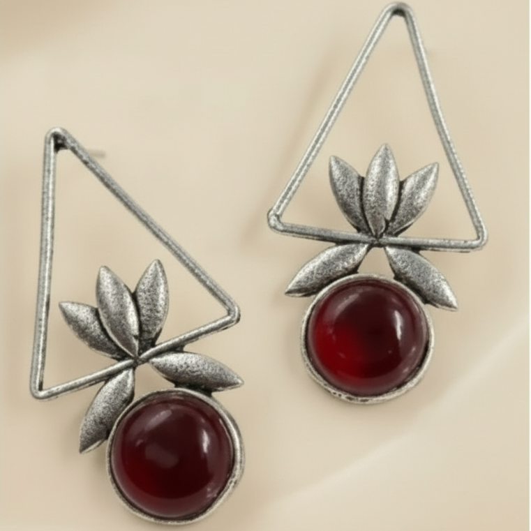 Pair of earrings with silver geometric designs and red stones on a white background