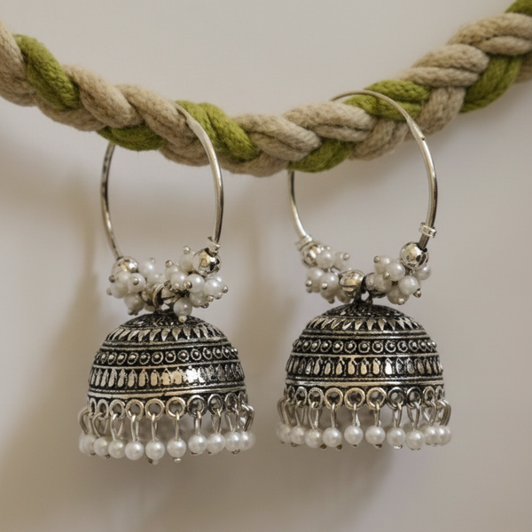 Pair of silver earrings with pearl accents hanging on a braided cord.
